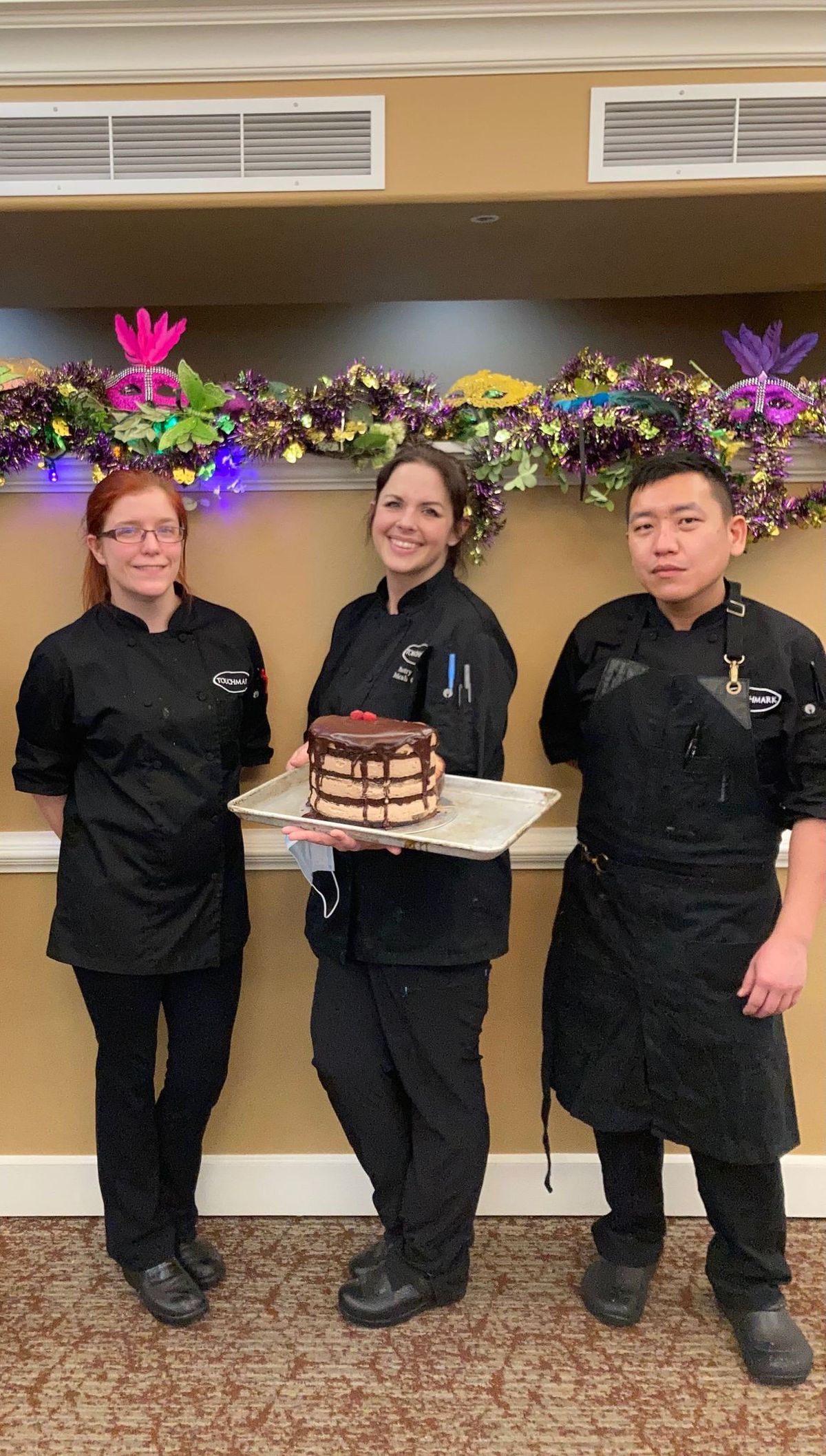 Micah Henderling, flanked by Bethany Meyer and Chong Vang, holds a chocolate ganache cake at Touchmark on South Hill.  (Kris Kilduff/For The Spokesman-Review)