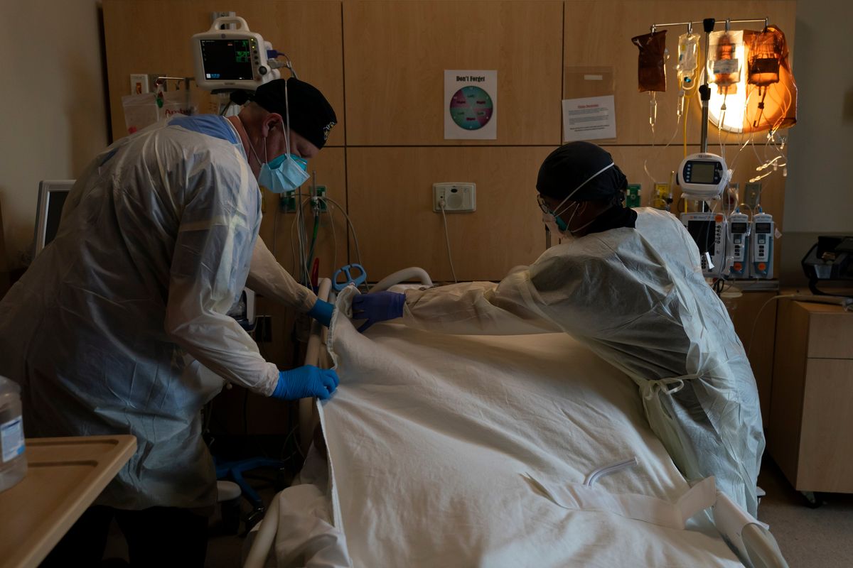 FILE - Respiratory therapist Frans Oudenaar, left, and registered nurse Bryan Hofilena cover a body of a COVID-19 patient with a sheet at Providence Holy Cross Medical Center in Los Angeles, Dec. 14, 2021. The fast-moving omicron variant may cause less severe disease on average, but COVID-19 deaths in the U.S. are climbing and modelers forecast 50,000 to 300,000 more Americans could die by the time the wave subsides in mid-March. (Jae C. Hong)