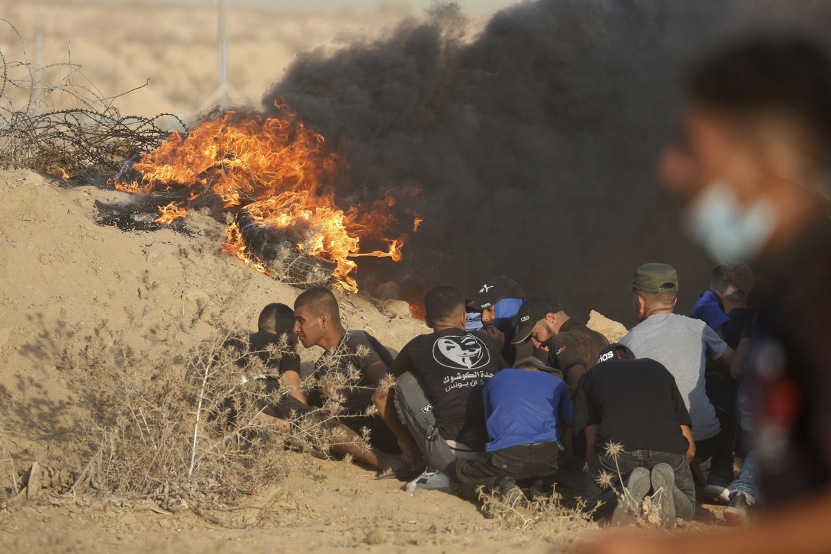 Protesters take cover next to tires on fire near the fence of Gaza Strip border with Israel during a protest east of Khan Younis, southern Gaza Strip, Wednesday, Aug. 25, 2021. Hundreds of Palestinians on Wednesday demonstrated near the Israeli border in the southern Gaza Strip, calling on Israel to ease a crippling blockade days after a similar gathering ended in deadly clashes with the Israeli army.  (Abdel Kareem Hana)