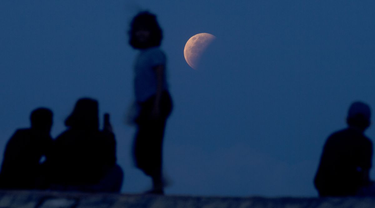 Residents watch the lunar eclipse at Sanur beach in Bali, Indonesia on Wednesday, May 26, 2021. The total lunar eclipse, also known as a super blood moon, is the first in two years with the reddish-orange color the result of all the sunrises and sunsets in Earth