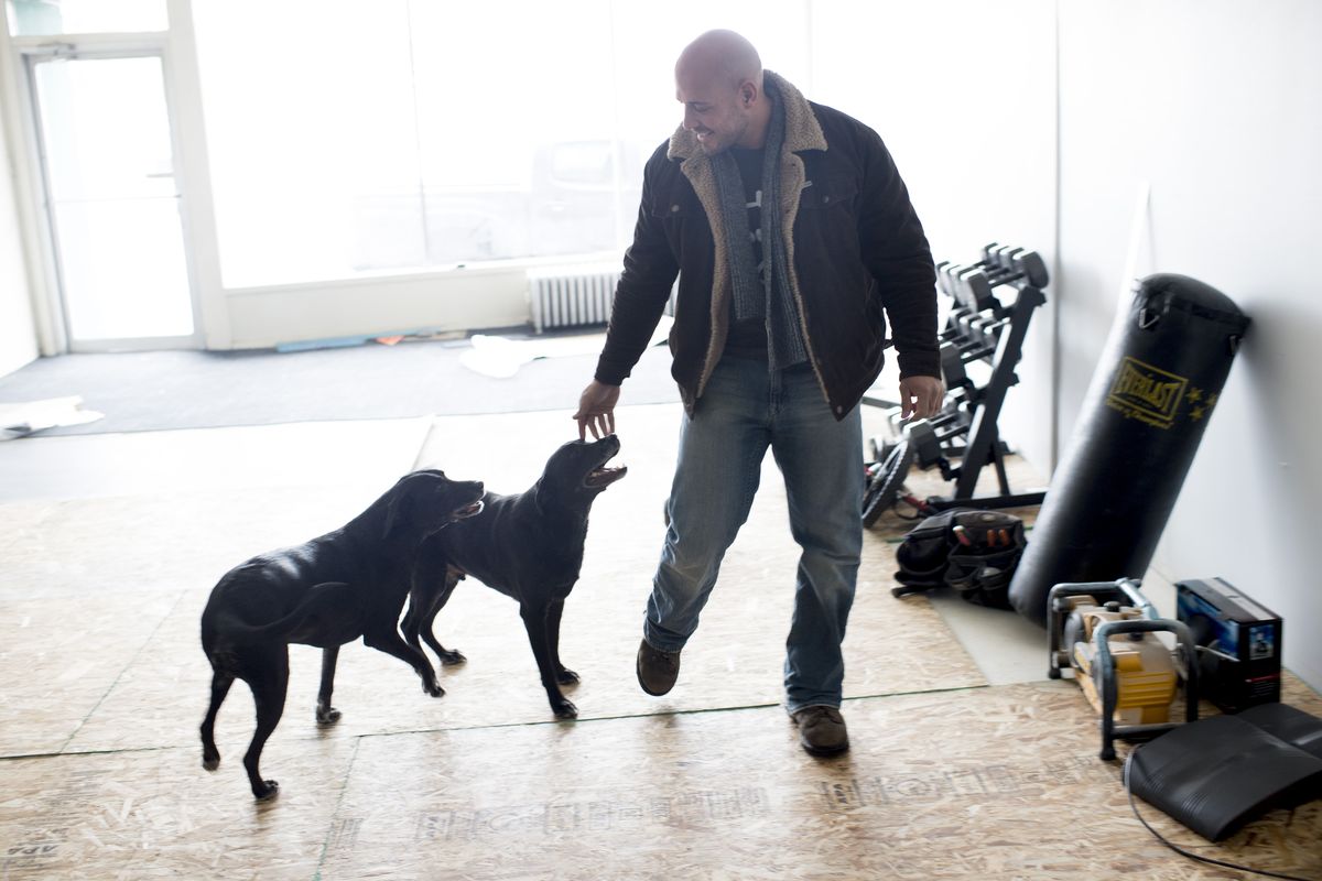 Shawn Kingsbury, founder of Pura Vida Recovery, a sobriety group that combines 12-step program with physical fitness, yoga and high-intensity training, pets therapy dogs Azul and Amor in a space he is renovating for the program on Jan. 2 in Spokane. (Tyler Tjomsland)