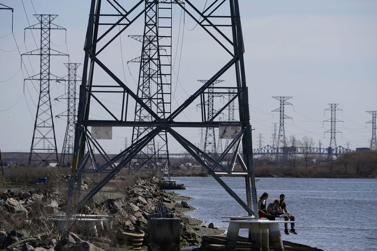 People sit at the base of a transmission tower in North Arlington, N.J., Tuesday, April 6, 2021. The Biden White House is amplifying the push for its $2.3 trillion infrastructure package with the release of state-by-state breakdowns that show the dire shape of roads, bridges, the power grid and housing affordability. Biden is scheduled to meet Monday, April 12, 2021 with Republican and Democratic lawmakers and can deploy the figures to show that his plan would help meet the needs of their constituents. (Seth Wenig)