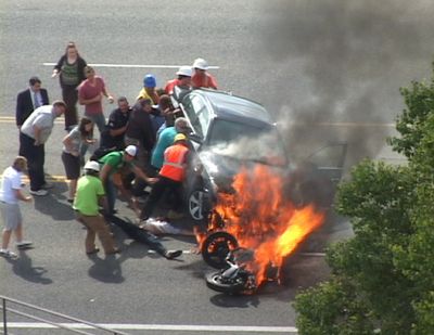 In this Monday, Sept. 12, 2011 image taken from video, a group of people tilt a burning BMW up to free Brandon Wright, on his back on the ground, who was pinned underneath after he collided with the car while riding his motorcycle on U.S. 89 in Logan, Utah.  Authorities said Wright was riding his motorcycle near the Utah State University campus in Logan when the 21-year-old collided with the BMW that was pulling out of a parking lot. Tire and skid marks on the highway indicate that Wright laid the bike down and slid along the road before colliding with the car, Assistant Police Chief Jeff Curtis said. (Chris Garff / Associated Press)