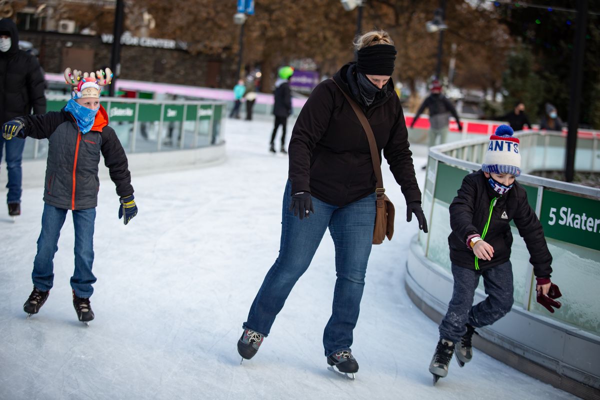 Owen Hartman, left, skates with his mother, Amber Hartman, while masked as another unidentified child zips by on the Numerica Skate Ribbon at Riverfront Park on Dec. 6. Opening day for the 2020 ice-skating season was Dec. 5.  (Libby Kamrowski/The Spokesman-Review)