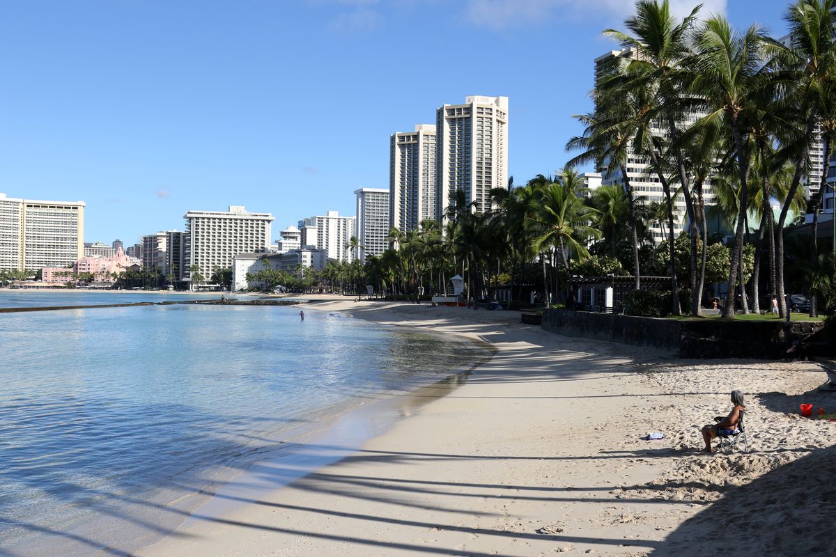 A man sits on a nearly empty Waikiki Beach in Honolulu, Friday, Oct. 2, 2020. After a summer marked by a surge of coronavirus cases in Hawaii, officials plan to reboot the tourism based economy later this month despite concerns about the state
