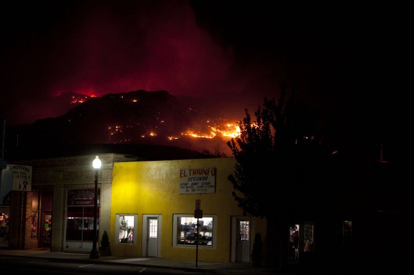 A wildfire is seen raging in the hills behind Brewster early Friday morning, June 18, 2014, in Brewster, Wash. (Tyler Tjomsland / The Spokesman-Review)