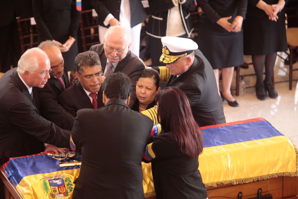 Venezuelan government officials join hands over the flag-draped casket of Venezuela