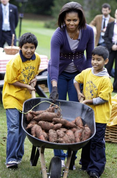 In this Oct. 29, file photo first lady Michelle Obama helps students from Washington, D.C.’s Bancroft Elementary School push a wheelbarrow with sweet potatoes that they harvested from her garden on the South Lawn of the White House.  (Associated Press)
