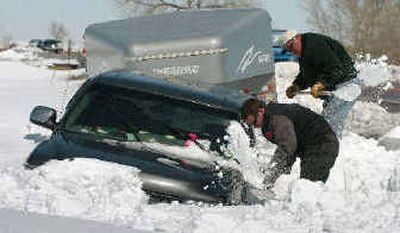 
Two men dig out a truck and trailer, used to transport show pigs, from a snowdrift Monday on U.S. Highway 24 northeast of Falcon, Colo. The 17 show pigs had to spend Sunday night in the trailer after the truck driver slid off the road. 
 (Associated Press / The Spokesman-Review)