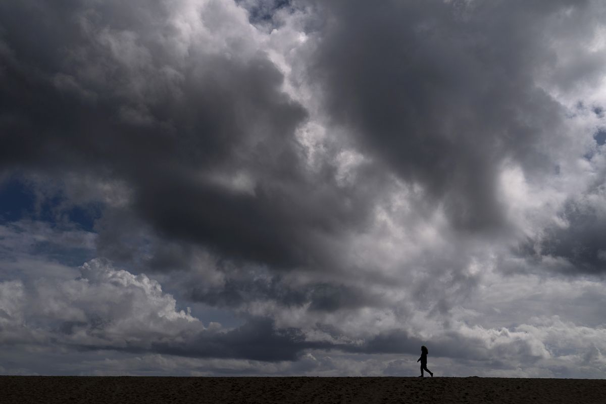 FILE - In this March 10, 2021, file photo, a woman strolls along the beach under rain clouds in Seal Beach, Calif. Rainstorms grew more erratic and droughts much longer across most of the U.S. West over the past half-century as climate change warmed the planet, according to a sweeping government study released, Tuesday, April 6, 2021, that concludes the situation in the region is worsening.  (Jae C. Hong)
