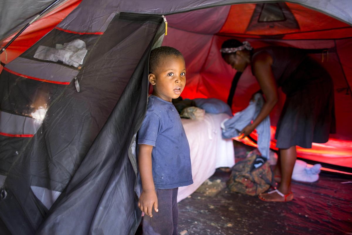In this Aug. 15, 2016, photo, Marlene Andre, 38, arranges clothes while her son, Johnsley, 5, stands in front of their tent in Jacmel, Haiti. Marlene was barely scraping by before a U.N. peacekeeper made her pregnant. The birth of her fourth child was the tipping point. She now cant afford rent and lives in a threadbare tent. (Dieu Nalio Chery / Associated Press)