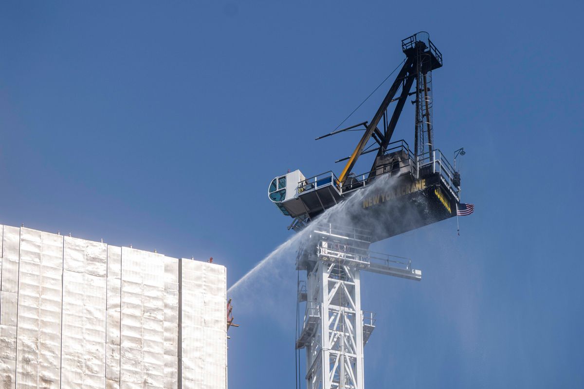 Water is sprayed on a tower crane that caught fire and partially collapsed 45 stories above the street at 550 10th Avenue in New York, July 26, 2023. Four civilians and two firefighters received minor injuries when the crane on 10th Avenue collapsed, officials said.    (Hiroko Masuike/The New York Times)